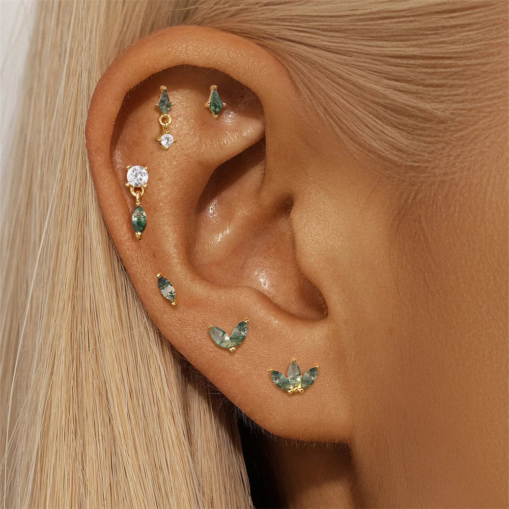 Close-up of an ear with multiple gemstone earrings on a neutral background