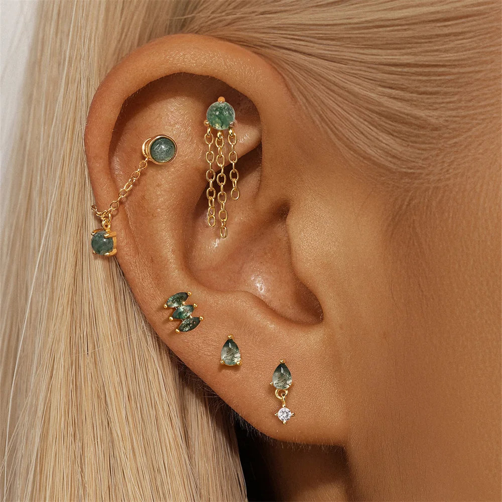 Close-up of an ear wearing gold earrings with green gemstones.