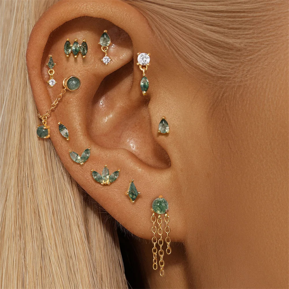 Close-up of an ear wearing multiple gold and green gemstone earrings.
