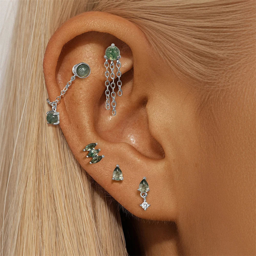 Close-up of an ear with multiple gemstone earrings on a neutral background