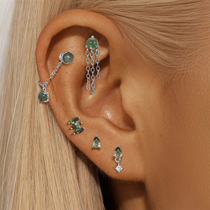 Close-up of an ear with multiple gemstone earrings on a neutral background