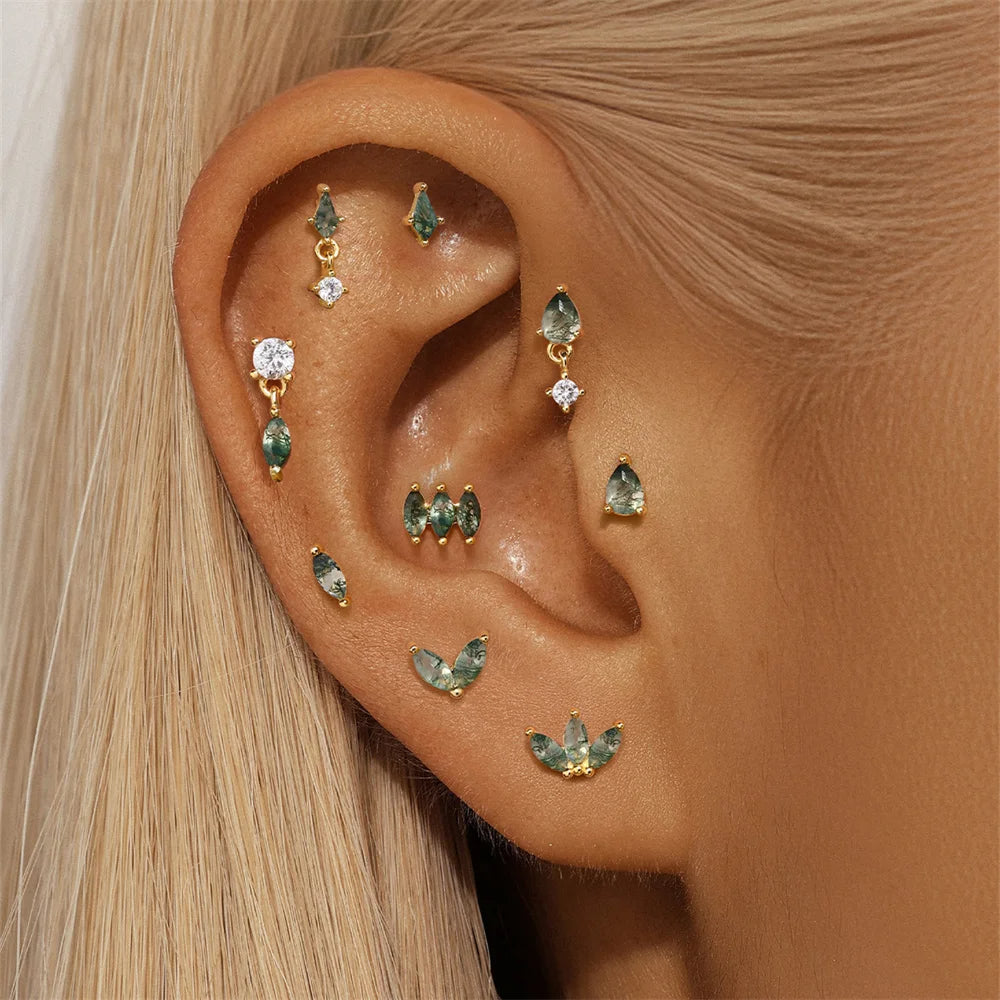 Close-up of an ear wearing multiple gold and green gemstone earrings.