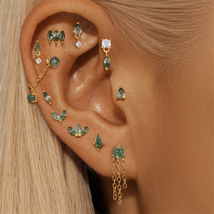 Close-up of an ear wearing multiple gold and green gemstone earrings.