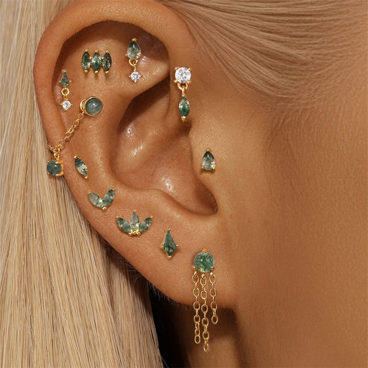 Close-up of an ear wearing multiple gold and green gemstone earrings.